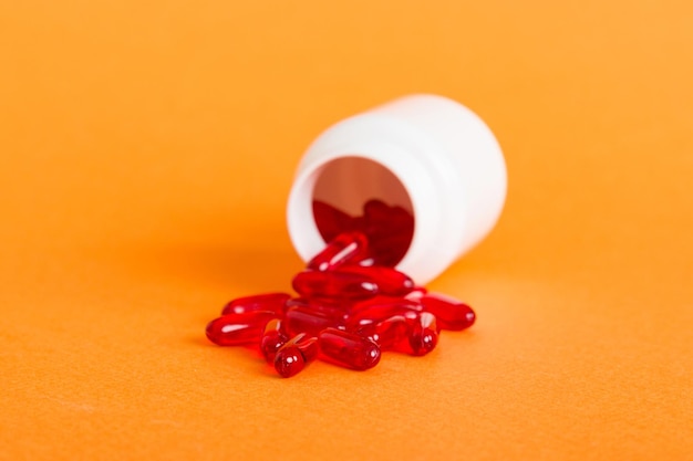 Red pills spilled around a pill bottle Medicines and prescription pills flat lay background Red medical capsules