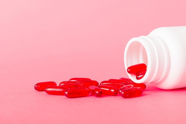 Red pills spilled around a pill bottle Medicines and prescription pills flat lay background Red medical capsules