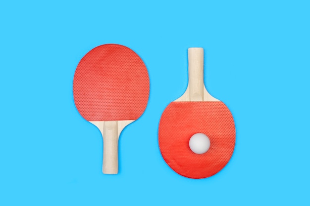 Red ping pong paddles and a white ball on blue