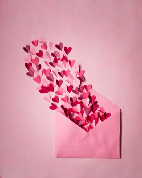 Red and pink paper hearts in open pink postal envelope on pink