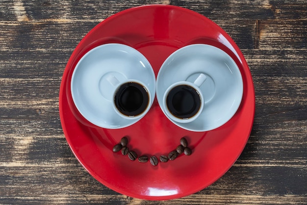 Red plate along with two cups of coffee and a smile from coffee beans on a wooden table Close up top view