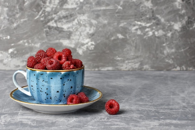 Red raspberries in a blue cup of copy space