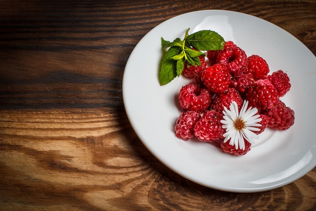 Red raspberries on a white plate on a wooden table