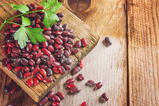 Red raw beans with greens on a wooden table.