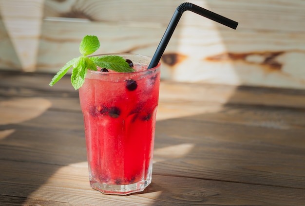 Red refreshing lemonade with berries and ice on a wooden table. Summer drink.