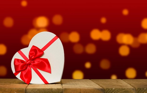 A red ribbon bow is placed on a wooden table with a red background.