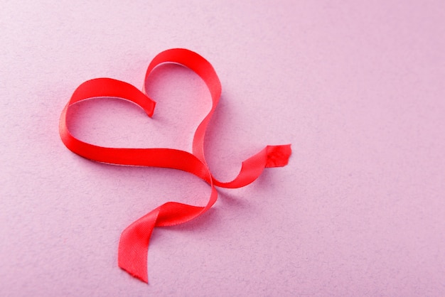 Red ribbon in shape of heart on light textured background