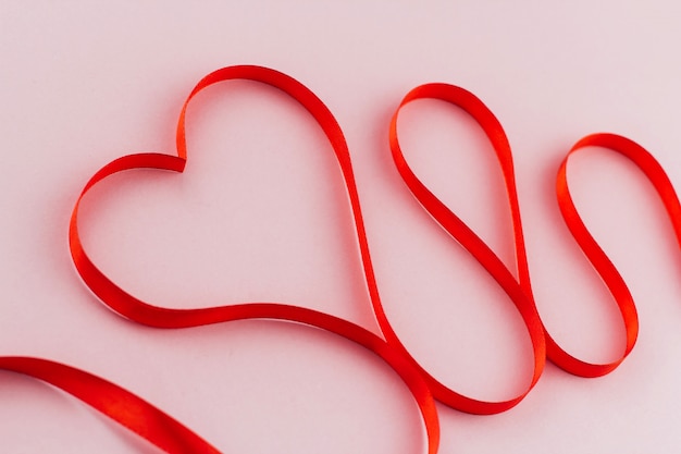 red ribbon in the shape of a heart on a pink background