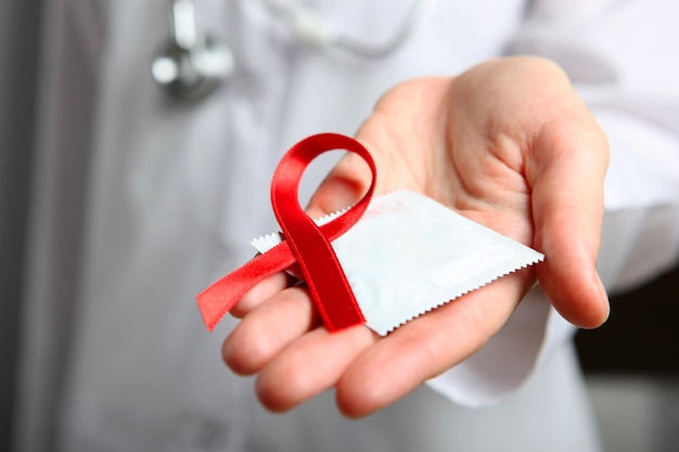 Red ribbon symbolizing aids and condoms in the hands of a doctor in a white coat