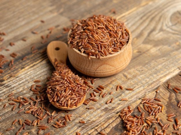 Red rice brown rice in a wooden bowl red rice scattered on the groundclose up