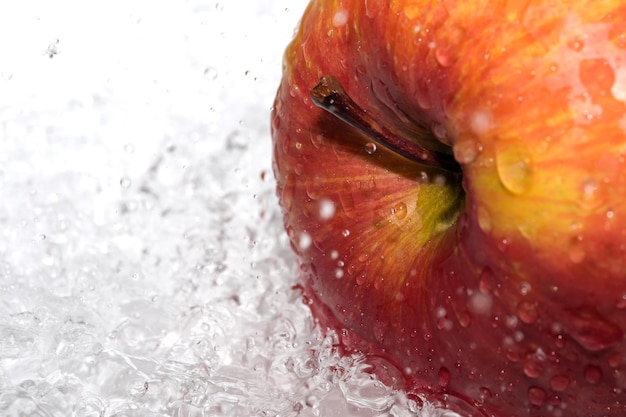 Red ripe sweet apple on a white plate poured with water from a shower sanitizing fruit close-up macro photography