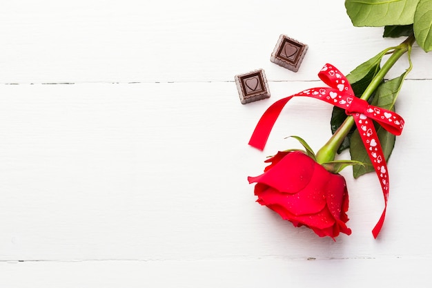 Red rose, chocolates on a white wooden background