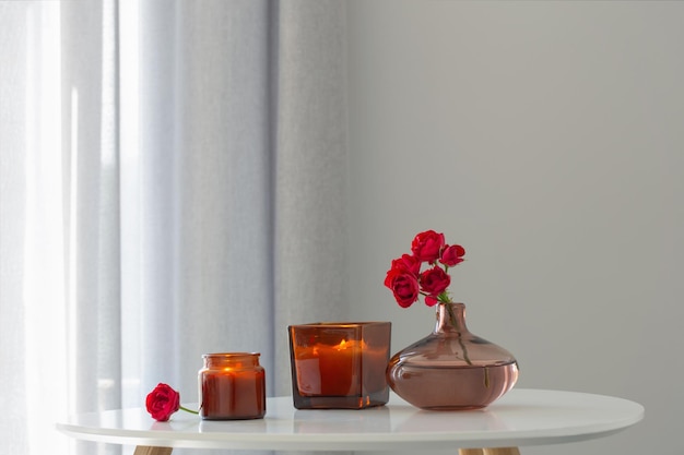 Red roses in vase with burning candles in white interior