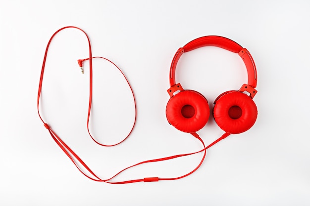 Red round headphones with cord forming frame flat lay on white background with copy space