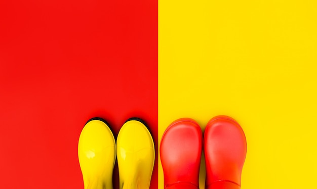 Red rubber boots on a yellow background and yellow boots on a red background stand side by side