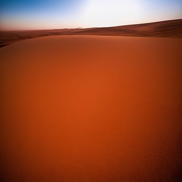 A red sand dune in the desert with the sun setting behind it.