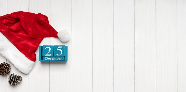 Red Santa Claus hat and blue perpetual calendar on white wooden background