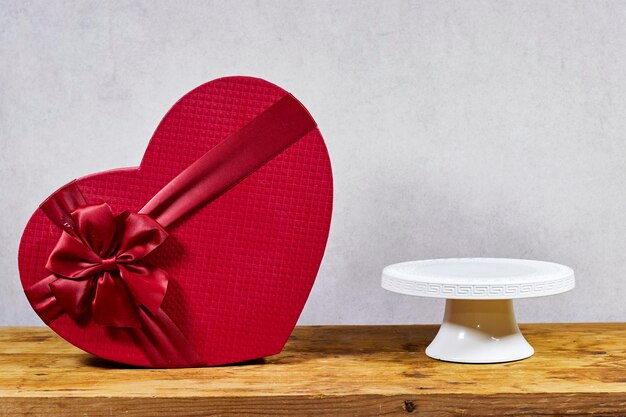 red shaped box with empty stand cake on wooden board near gray grunge background for valentines