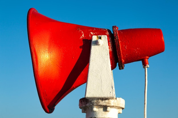 A red ship's horn is fixed on a steel rack against a blue sky