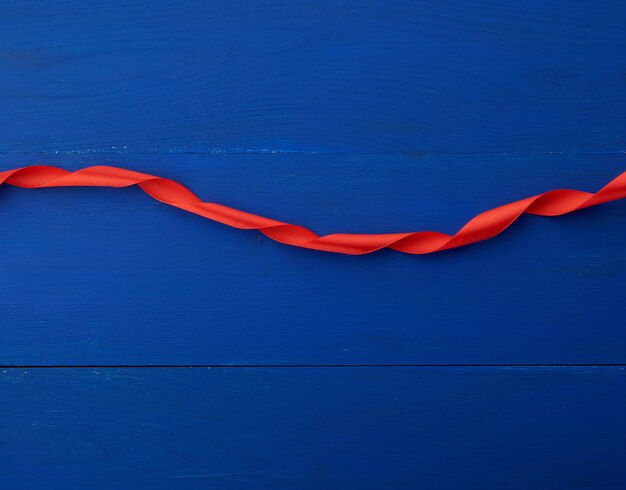 Photo red silk thin ribbon twisted on a blue wooden background