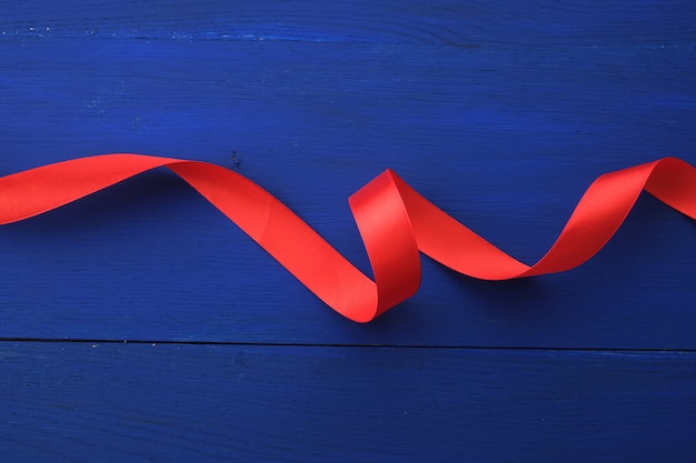 Red silk thin ribbon twisted on a blue wooden background