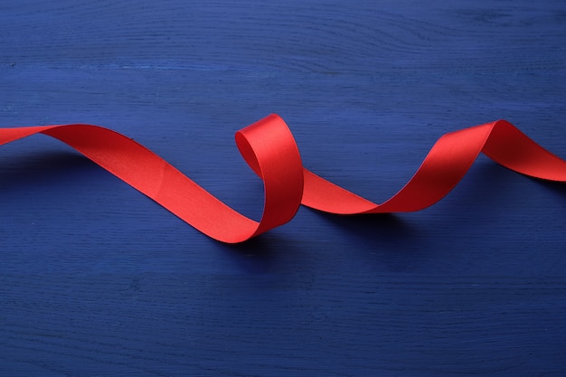 Red silk thin ribbon twisted on a blue wooden background