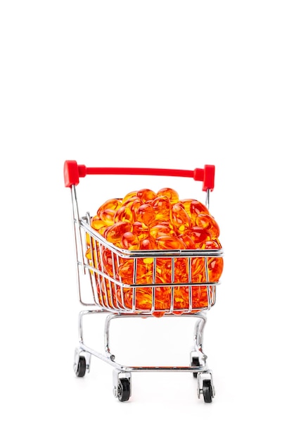 Red soft gel vitamin capsules in mini supermarket push cart isolated on white background, healthy and marketing concept