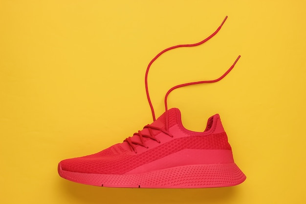 Red sport running shoe with untied laces on yellow background