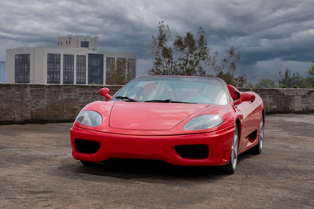 Red sports car on a city rooftop with buildings and cloudy sky in the background