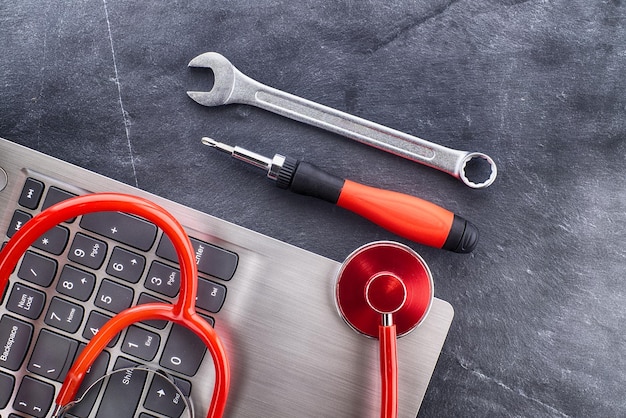 Red stethoscope on top of a laptop near screwdriver and spanner