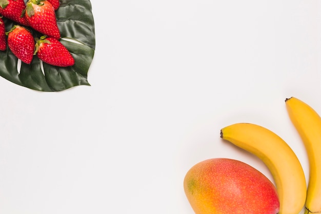 Red strawberries on monstera and banana with mango in corner on white background