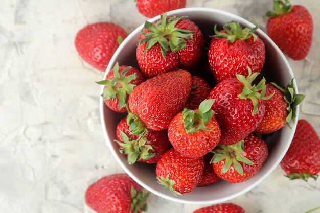 Red strawberry in a ceramic bowl on a light concrete table, top view