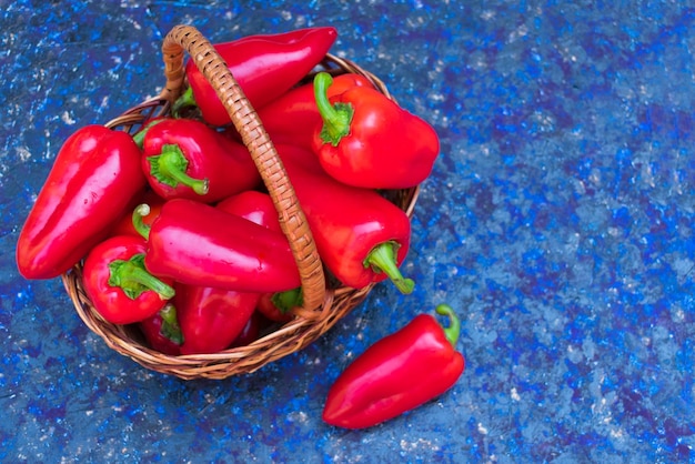 Red (sweet) bell peppers in a wicker basket on a blue background. Copy space Top view.