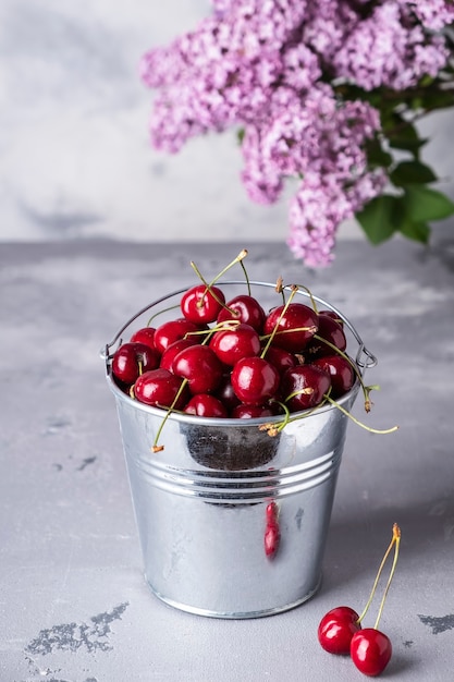 Red sweet cherry in metal bucket on gray table.