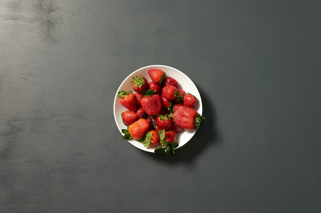 Red sweet ripe strawberries in a white plate on gray wall background