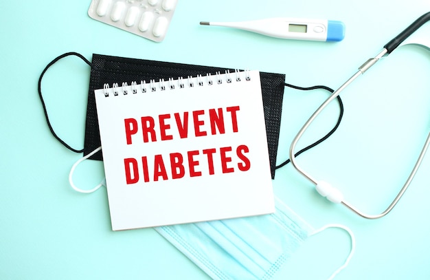 The red text prevent diabetes is written on a notepad that sits on a blue background next to medical