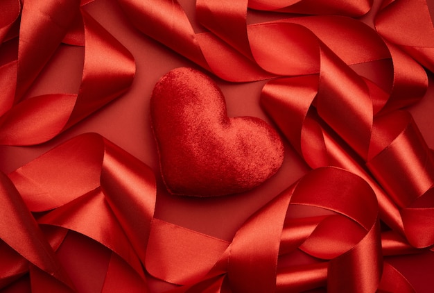 Red textile heart and curled red silk ribbon on a red background, festive background, top view