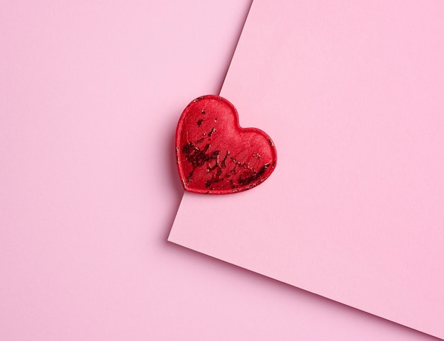 Red textile heart on a pink paper background top view