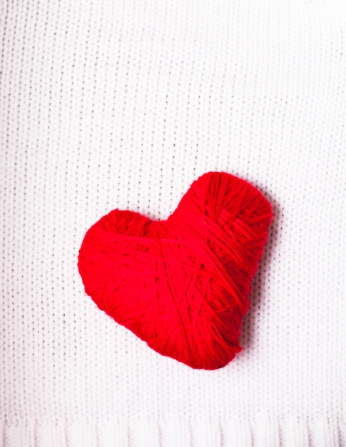 Red thread heart over knitted white textile. Valentine background