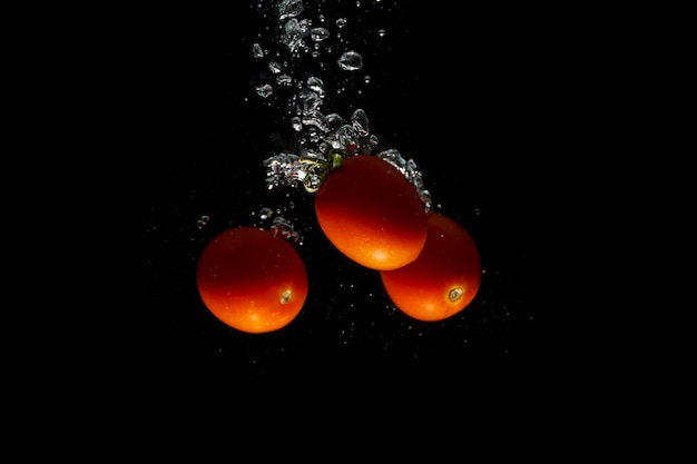 Red tomato on black background with water splash