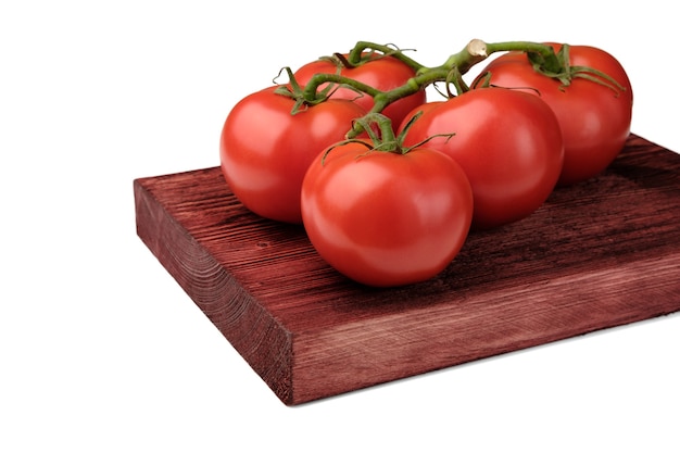 Red tomatoes on a green branch lie on a painted wooden board and are isolated on a clean white background.