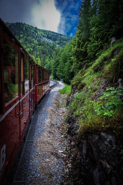 Red tourist train running lying across mountains with foggy backgroundAustria