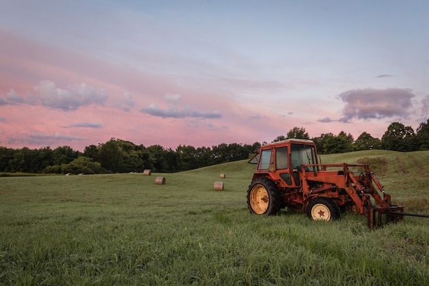 Red tractor and freshly rolled hay bales in a farmland at sunset