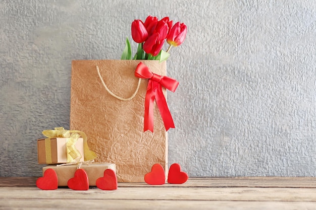 Red tulips in paper bag on wooden table against the grey wall close up