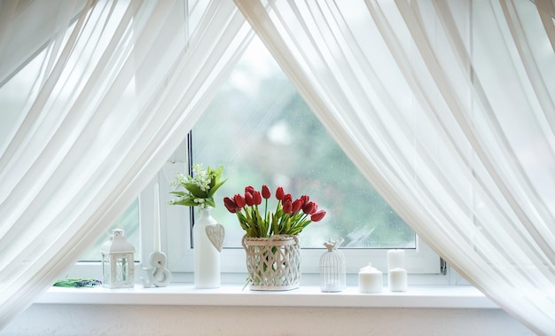 Red tulips and snowdrops in basket on the windowsill