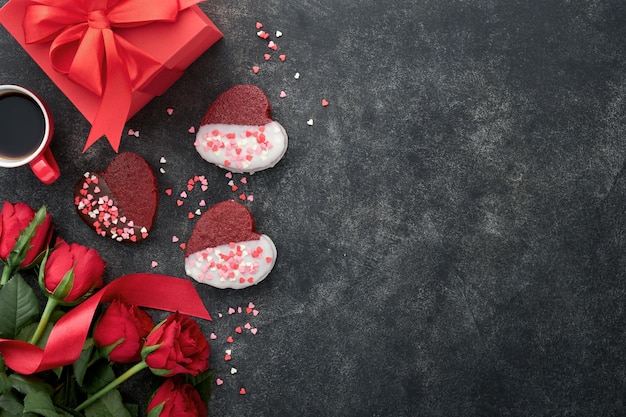 Red velvet or brownie cookies on heart shaped in chocolate icing with red roses and gift box on black background Dessert idea for Valentines Day Mothers or Womens Day Dessert for Valentines Day