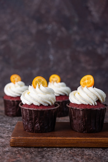 Red velvet cupcakes with white cream on top decorated with kumquat slice.