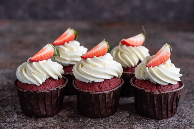 Red velvet cupcakes with white cream on top decorated with strawberry slice.