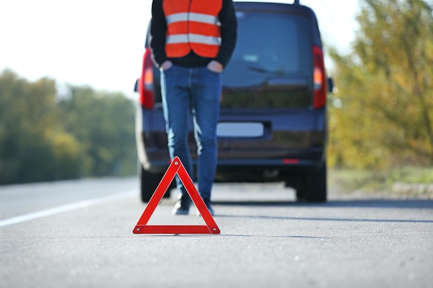 Red warning triangle on asphalt road Tow truck worker near broken down car