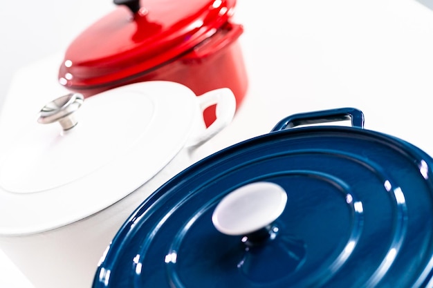 Red, white and blue enameled cast iron covered round dutch ovens on a whjite background.